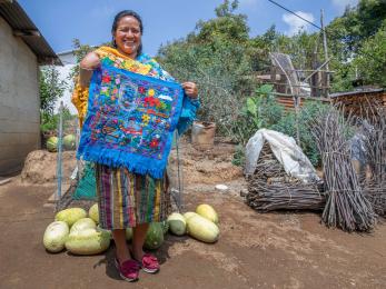 A person holding a brightly colored piece of clothing they made by hand.